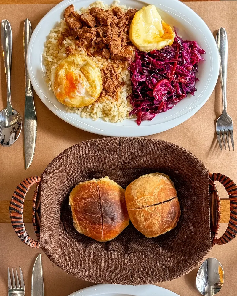 Top-down view of the Champions Breakfast (rice, goulash, fried egg, kashkaval, red cabbage), a bread basket and Grandma's Coddling