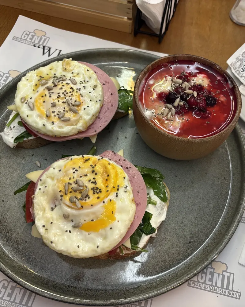Fried eggs on toast with ham and greens, and a bowl of yogurt with berries