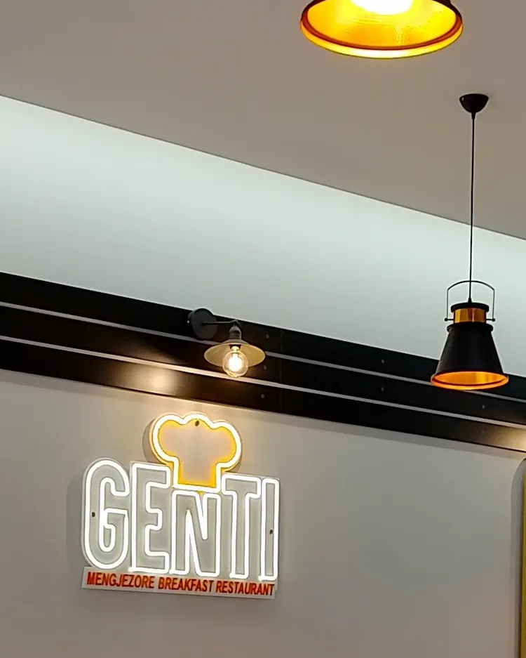 Black pendant lamps with brass interiors above the glowing Genti neon sign