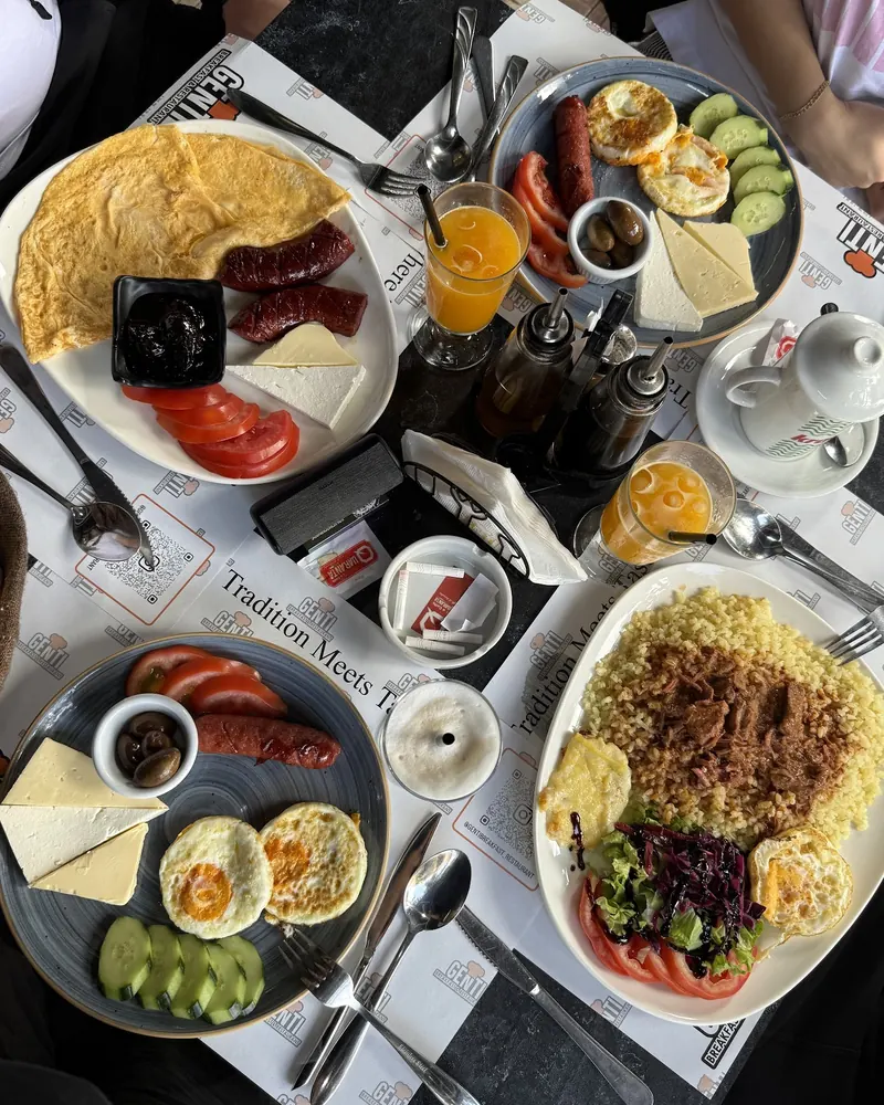 A breakfast table with omelette, sausages, cheese, eggs, rice and fresh juice